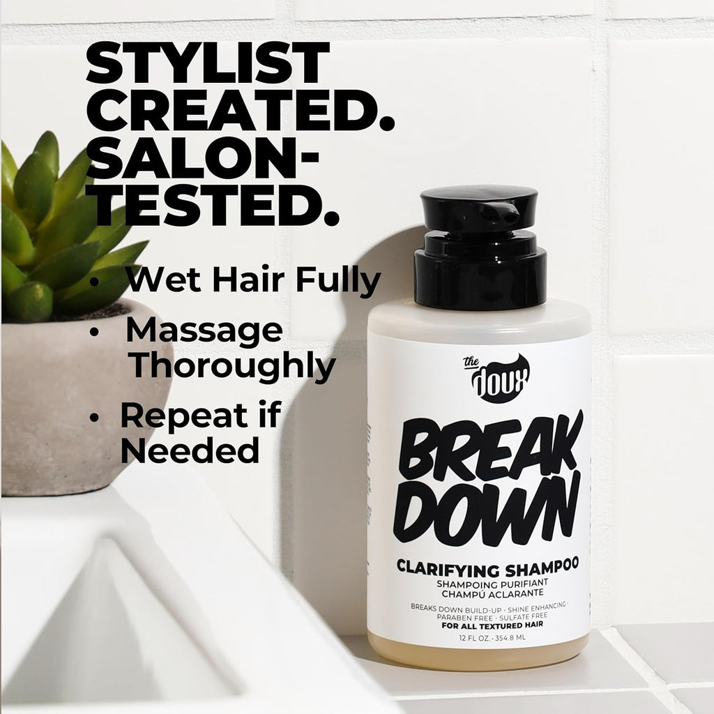 Bottle of 'The Doux Break Down Clarifying Shampoo' on a bathroom counter with text about usage.